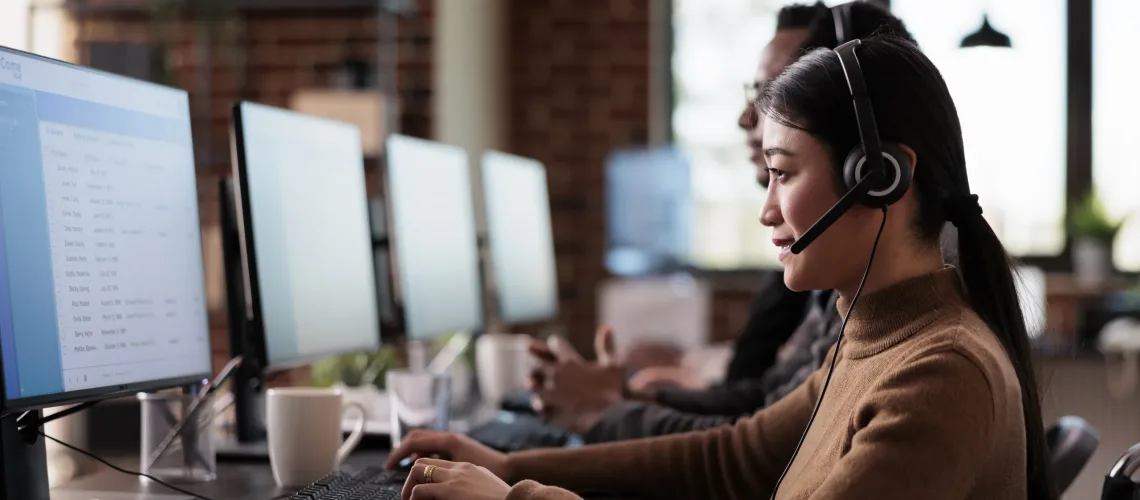 Paralyzed asian employee working at call center reception in disability friendly office. Female operator wheelchair user with impairment giving assistance on customer service helpline.